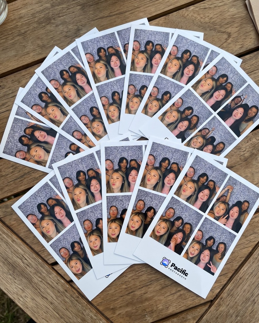 Pacific Photobooth 4x6 prints fanned out on a wooden table, each with four photos of friends in front of a sequin backdrop